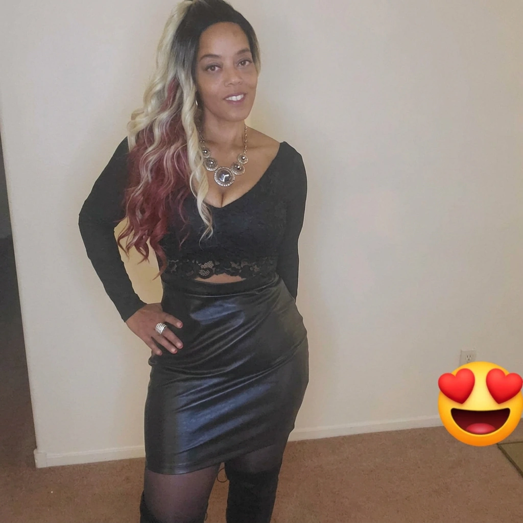 Woman with long blonde and burgundy waves wearing a black outfit and statement necklace